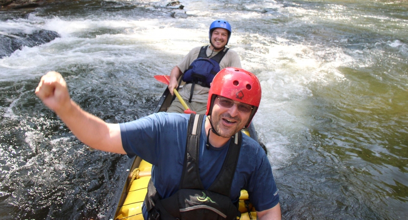 Two people wearing safety gear smile from inside a watercraft. 